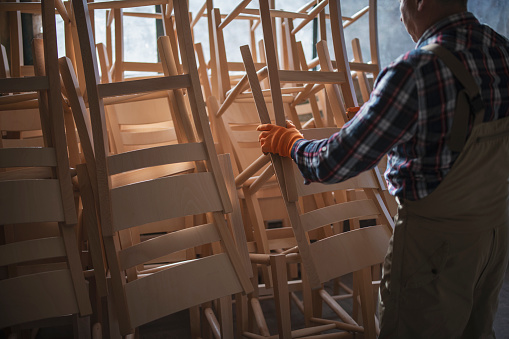 Carpenter arrange ready wooden chairs in workshop.