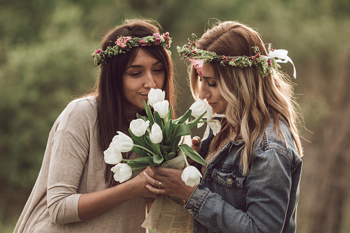 Two women with floral crowns smelling bouquet of tulips outdoors