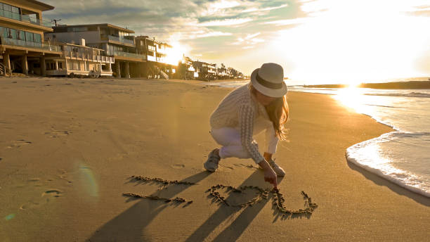 Attractive woman writing romantic message in the sand on the beach