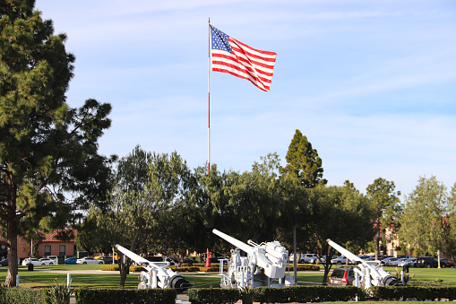 San Diego CA 1-30-2020  Large American flag flying next to old former Navy 50 caliber guns on display at the Liberty Station Park in San Diego