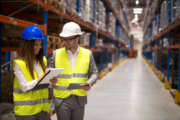 istock Warehouse managers sharing ideas and consulting each other about organization and distribution of goods. Business people wearing reflective vest and hardhat controlling inventory. 1204342958