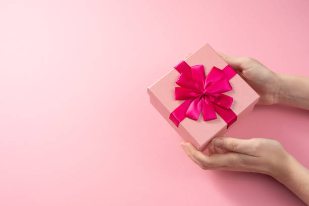 istock Valentine's Day celebration concept. A nice gift from a loved one. Box with a bow in female hands on a delicate pink background. Copy space. Flat lay. 1204343709