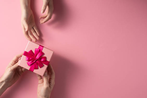 Valentine's Day celebration concept. A nice gift from a loved one. Box with a bow hands of a man and a woman on a delicate pink background. Copy space. Flat lay.
