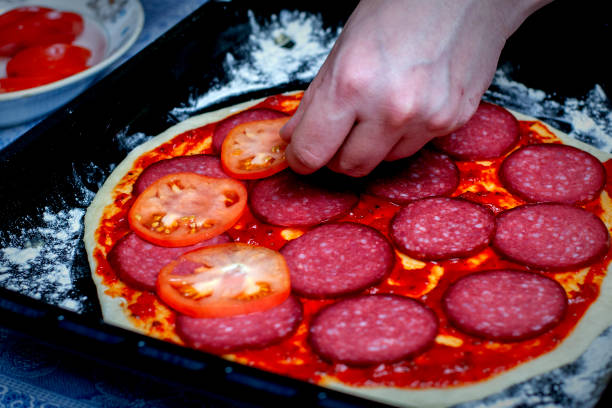 aplicação de tomates na massa de pizza. cozinhando pizza. o cozinheiro coloca o recheio na massa. pizza caseira. - pizza sauces chef making - fotografias e filmes do acervo