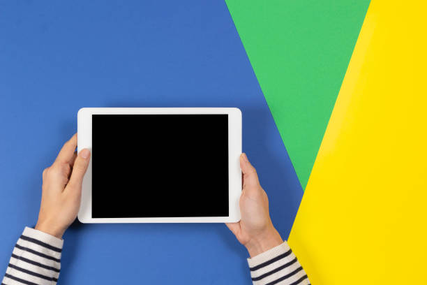 istock Female hands with digital tablet computer on blue yellow and light green background. Top view 1204348089