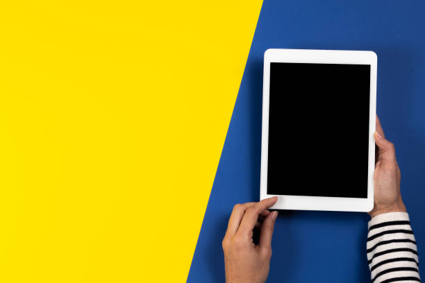 istock Female hands with digital tablet computer on navy blue and yellow background. Top view 1204348106
