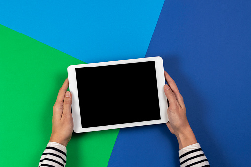 Female hands holding digital tablet computer on navy blue and light green background. Top view