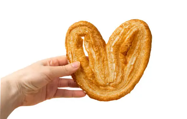 Hand holding palmiers pastry, palm heart or elephant ear isolated on white background. French puff pastry or pate feuilletee