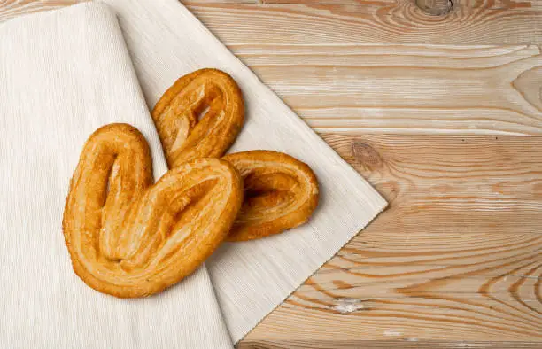 Sweet braided palmiers pastry, palm heart or elephant ear on wooden table desk background. French puff pastry or pate feuilletee top view with copy space