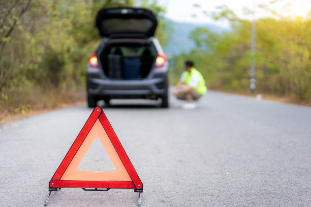 signe de triangle de panne sur la route avec l’homme asiatique inquiété réparant et changeant le pneu en attendant l’assurance ou la compagnie de centre de service de voiture viennent après la panne de voiture sur la route de campagne à l’arriè - automotive repair center photos et images de collection