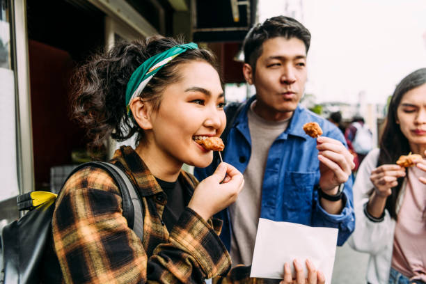 wesoła młoda kobieta jedząca jedzenie uliczne z przyjaciółmi - tasting zdjęcia i obrazy z banku zdjęć