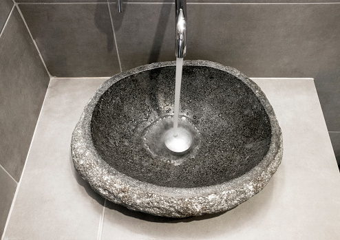 Top view of gray color stone sink with water running from tap in bathroom.