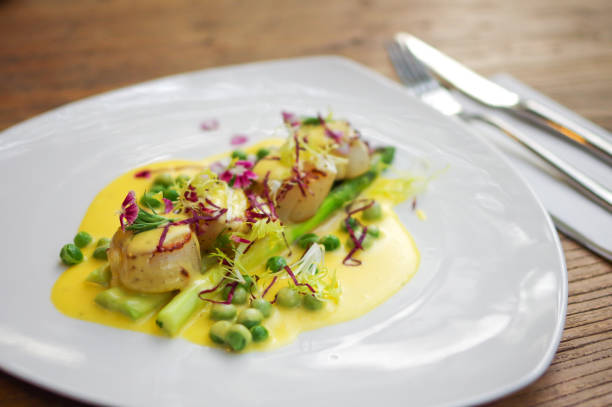 vieiras a la plancha con salsa amarilla, repollo púrpura rallado, guisantes verdes y flores en plato de triángulo blanco sobre mesa de madera - cabbage close up food fork fotografías e imágenes de stock