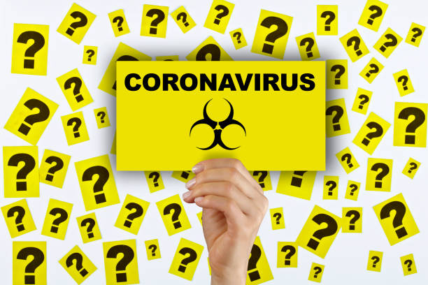 Woman hand holding corona virus sign. Question marks on the background. Woman hand holding corona virus sign. Lots of question marks on the white background. hazard sign photos stock pictures, royalty-free photos & images