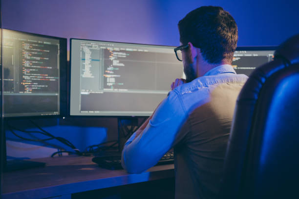 istock Rear back behind view portrait of nice focused skilled experienced guy thinking bug fixing debugging hardware software trouble shooting data secure blockchain in dark room workplace station 1204374576