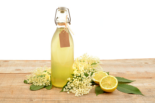 Homemade elderflower syrup in a bottle with flower (Sambucus nigra) and lemon on wooden table.
