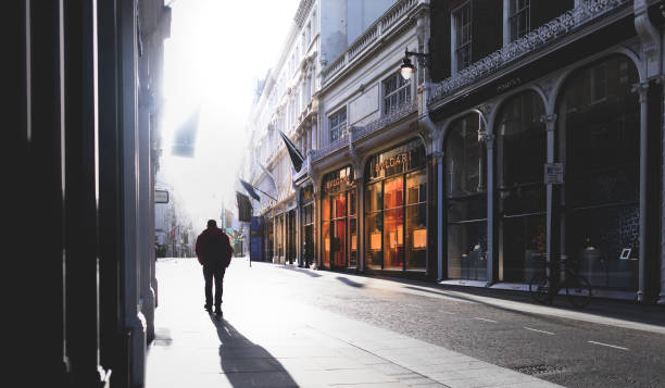 silhouetted man walking into the early morning sunshine, walking down new bond street in mayfair in central london with the high end retailer bulgari shop front warm glow standing out against the heavy morning shadows - bulgari imagens e fotografias de stock