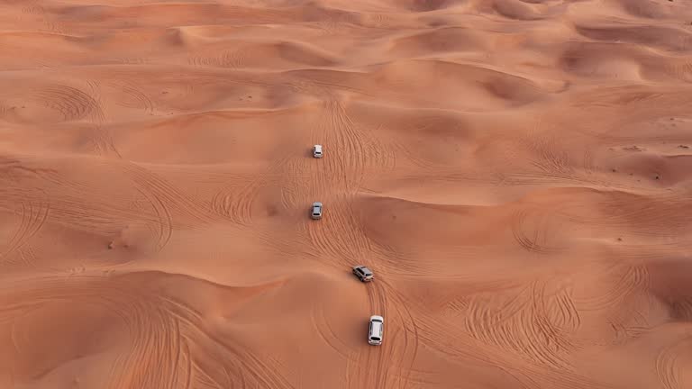 AERIAL. Column of white cars travelling in sand desert.