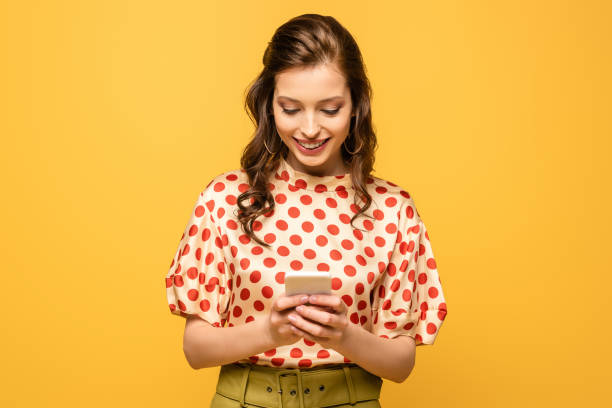 istock happy young woman smiling while chatting on smartphone isolated on yellow 1204387510