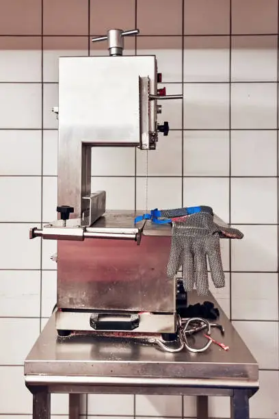 Bandsaw machine for cutting meat and a chainmail glove for protection in a slaughterhouse. Butchery equipment.