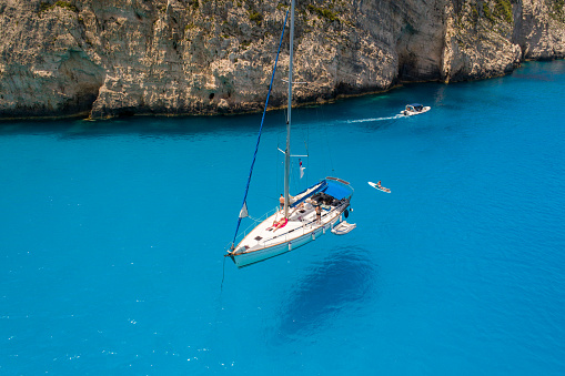 People relaxing and enjoying on sailboat moored in bay with beautiful color of water. This bay is next to the one of the most popular beach on the world, recognizable by turquoise color of water and smuggler's ship that left as wreck. Aerial view photos made with drone. Navagio beach, Zakynthos, Greece