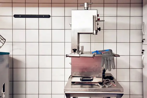 Bandsaw machine for cutting meat and a chainmail glove for protection in a slaughterhouse. Butchery equipment.