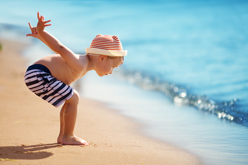 Happy boy jumping and playing at sea in straw hat. Child on vacation in summer at the beach
