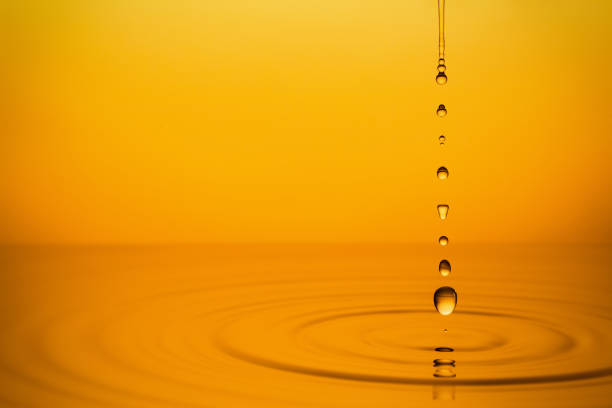 Ripple of the golden surface of yellow liquid with drops.