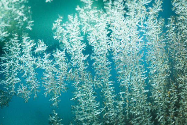 Close up macro color image depicting an abstract pattern of ice, snowflakes and frost on a glass surface. Room for copy space.