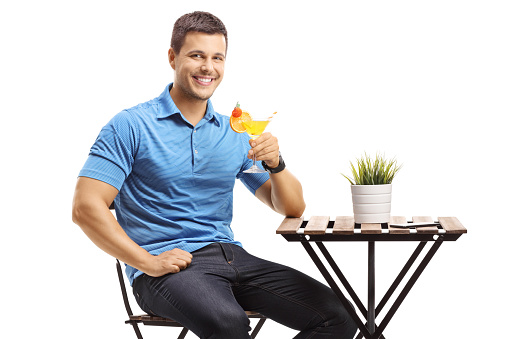 Guy sitting at a table and drinking a cocktail isolated on white background