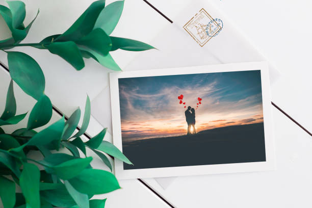 istock Photo postcard love hearts letter. Open envelope romantic message on white wooden table with green leaves. White card stamp. 1204395802