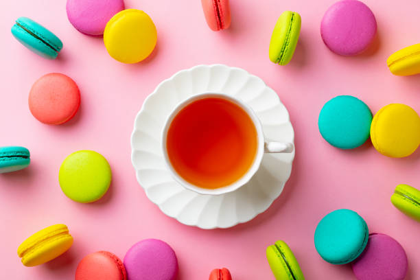 Macaroons dessert and cup of tea on pink pastel background. Top view.