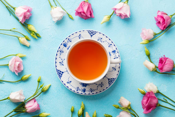 istock Cup of tea with pink flowers eustoma on blue background. Flat lay composition. Top view. 1204399355