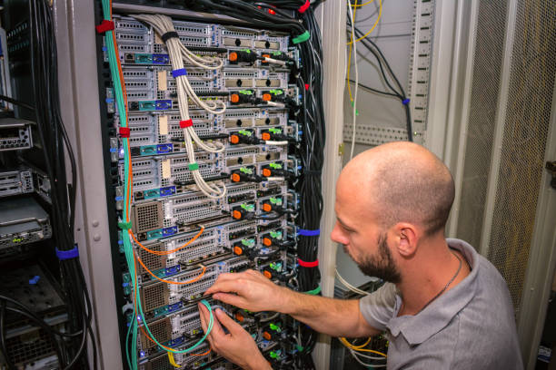 un spécialiste connecte les fils dans la salle des serveurs du centre de données. un homme travaille avec les télécommunications. le technicien change le câble internet des routeurs puissants - network server data center installing photos et images de collection