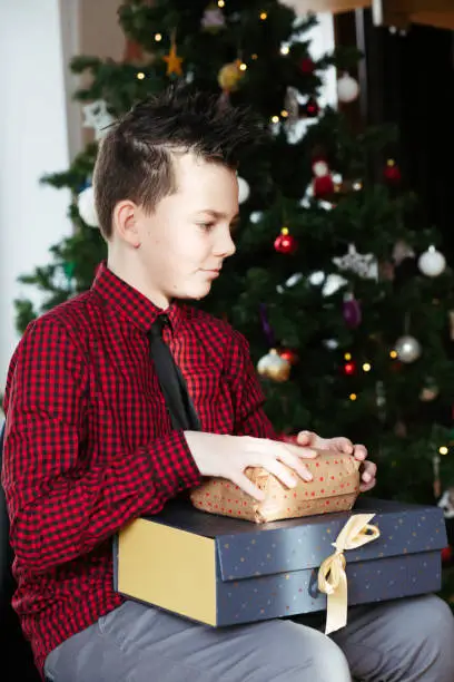 January 12, 2020 - Warsaw, Poland: funny handsome adolescent boy sitting on a chair with Christmas presents