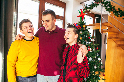 January 12, 2020 - Warsaw, Poland: father and two teenager sons embrace each other standing in front of Christmas tree