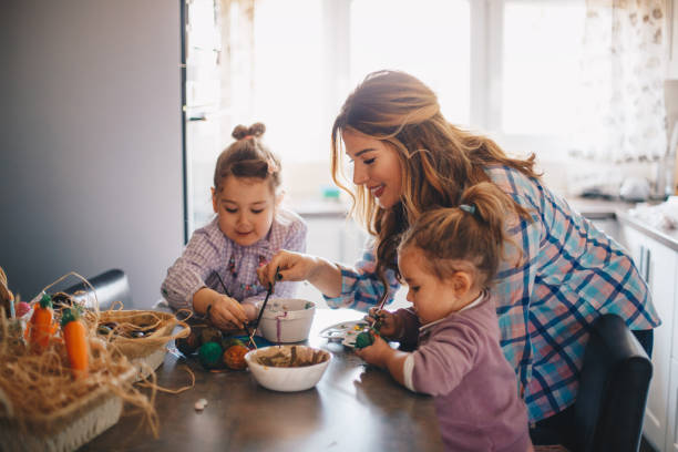 istock Two girls and their mother painting eggs for Easter at their kitchen. 1204403129