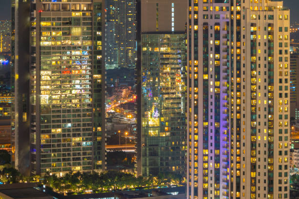 istock Pattern of office buildings windows illuminated at night. Lighting with Glass architecture facade design with reflection in urban city, Downtown Singapore City in financial district. 1204404925