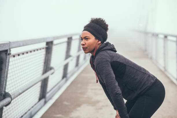 istock A young woman standing on a bridge walkway, resting from a jogging session. She is wearing headphones. 1204406396