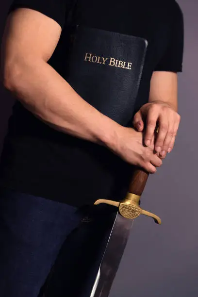 Casually dressed strong young guy standing ready with his Bible and sword