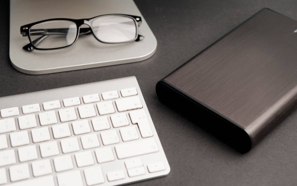 istock Black external hard drive and partial computer view, keyboard, black glasses, black background 1204414868