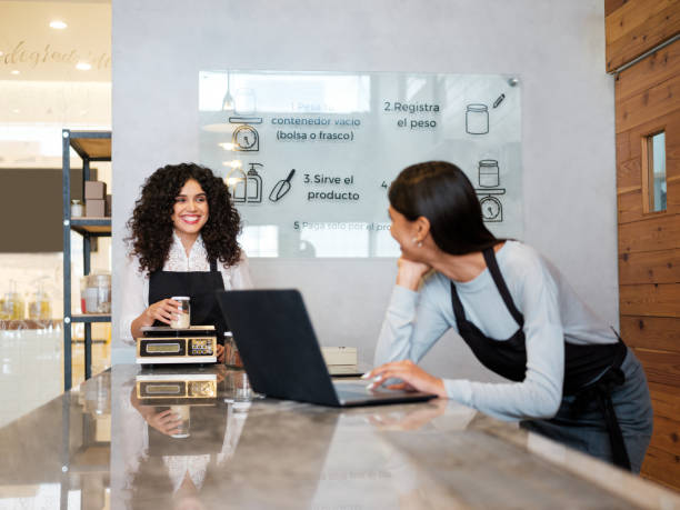 istock Two young female shop assistants smiling at each other at work 1204417207