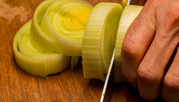 istock Human hand cutting and slicing fresh organic leek with a sharp kitchen knife on a wooden cutting board 1204417541