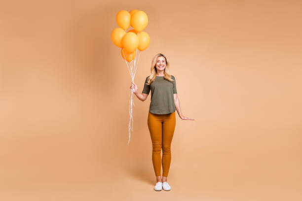 full längd foto av fantastiska charmiga blond dam som håller många ljusa orange luft ballonger kom till födelsedagsfest bära grön t-shirt byxor isolerade beige färg bakgrund - kvinna ballonger bildbanksfoton och bilder