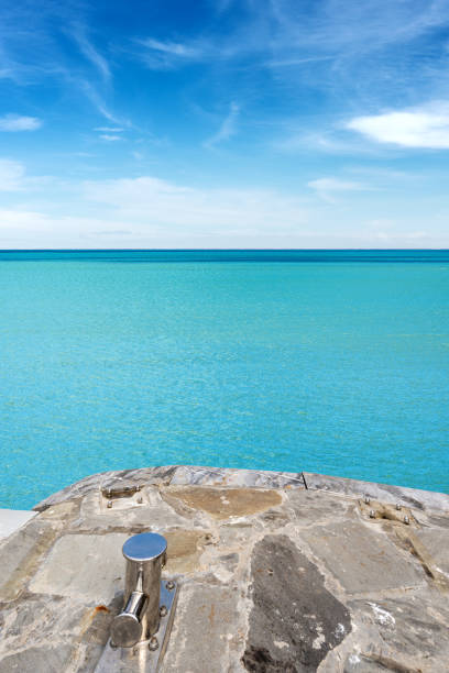Stone jetty with an empty mooring bollard and turquoise seascape with blue sky and clouds