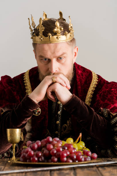 istock thoughtful king with crown sitting at table isolated on grey 1204426832