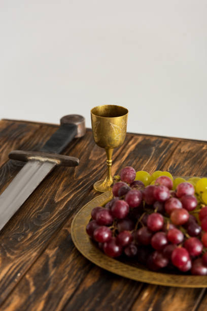istock ancient cup, sword and grape on wooden table isolated on grey 1204426836