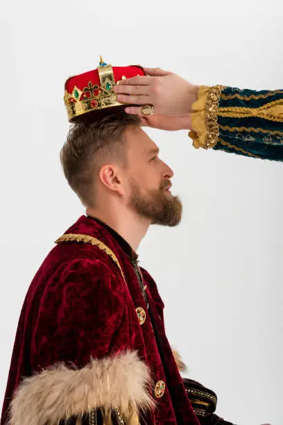 cropped view of man putting crown on king on grey background