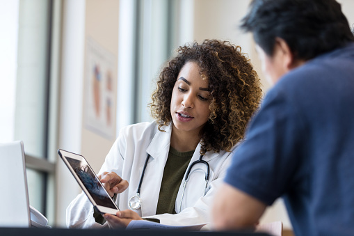 The mid adult female doctor uses the digital tablet to show the x-ray to the unrecognizable senior man.