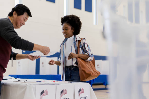 mature male volunteer explains voting document to young woman - jovens a votar imagens e fotografias de stock